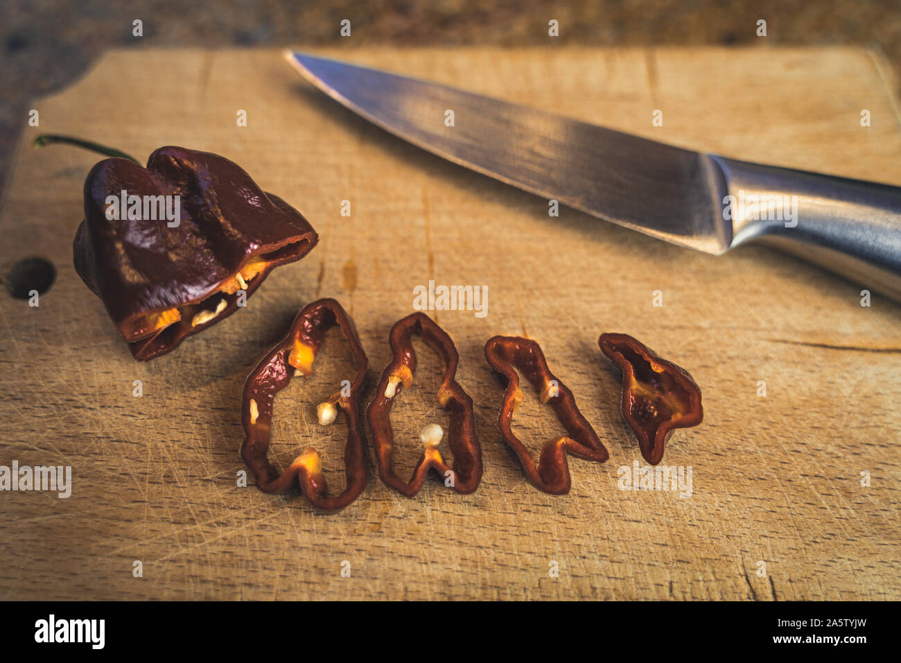 Chocolate Habanero pepper (Capsicum chinense) slices on a wood cutting board and a chrome knife. Healthy and really hot chili peppers. Stock Photo