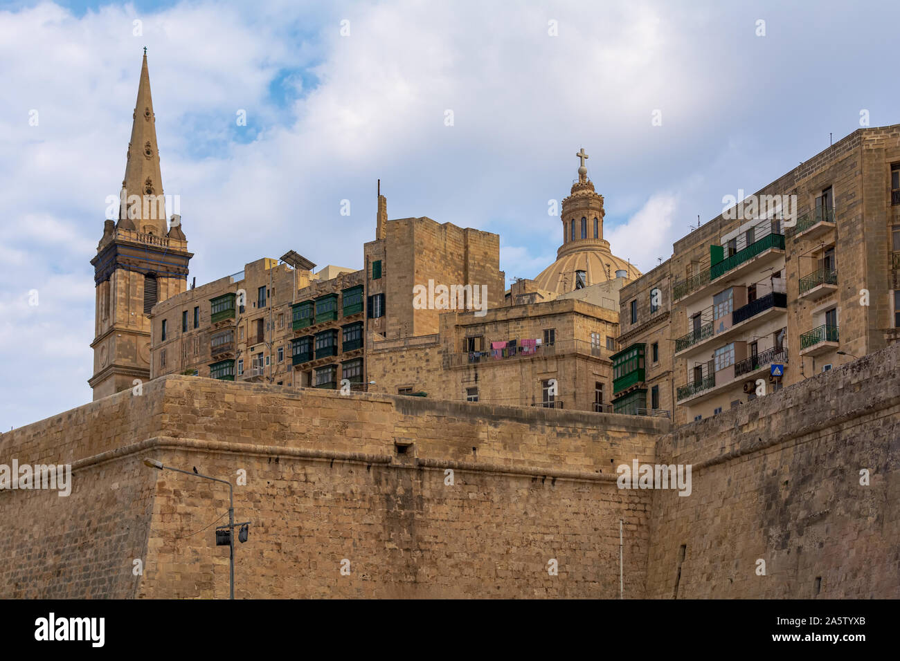 Valletta fortification wall and city famous buildings shot from ferry port. Tower of St. Paul's Anglican Cathedral and top of Carmelite Church's dome Stock Photo