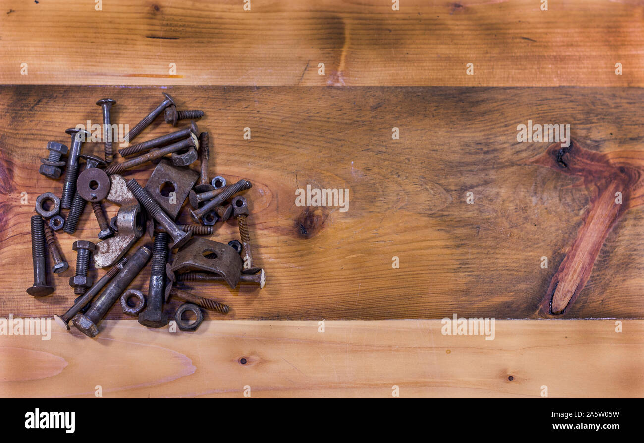 Wooden table background with rusty screws and bolts on the left side. Empty space on the right side. Top view. Stock Photo