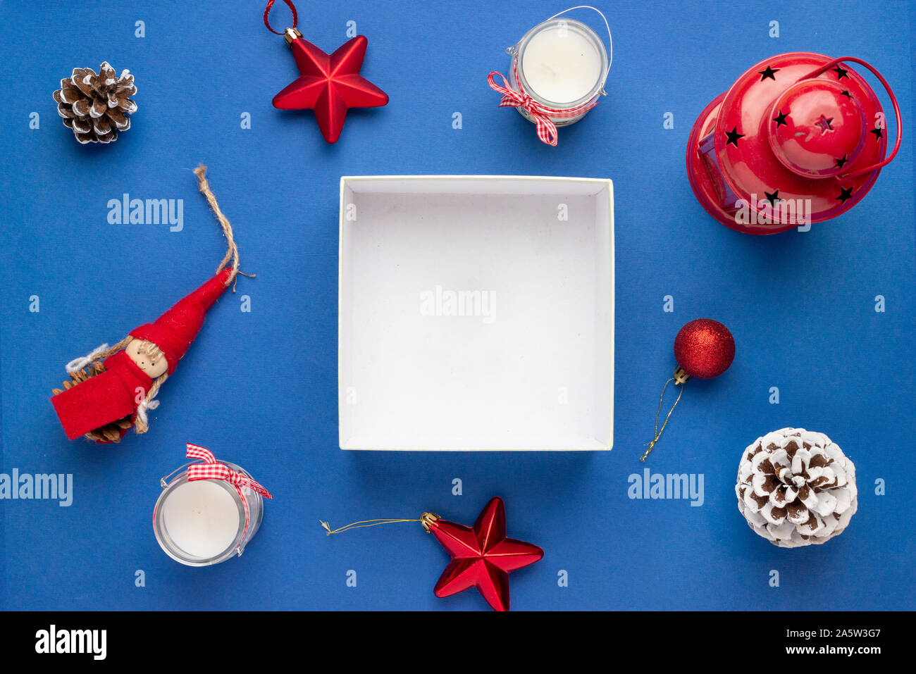 Empty gift box surrounded with Christmas decorations. Copy space on white gift box surface. Top view, flat lay, composition. Stock Photo