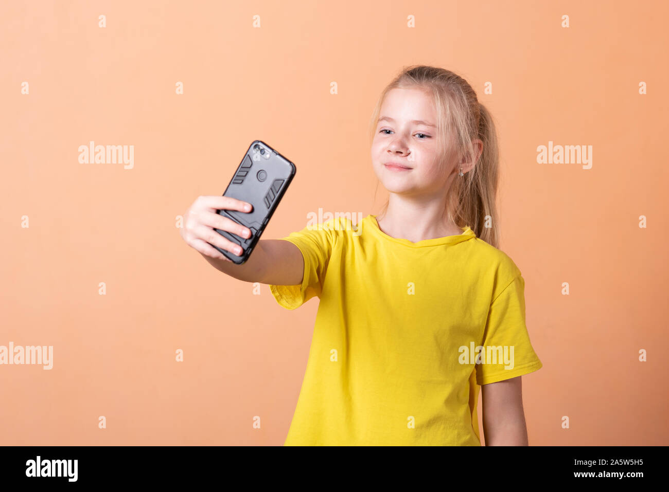 Little girl takes a selfie, on a light orange background. Stock Photo