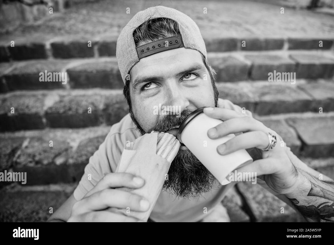 Man bearded eat tasty sausage. Urban lifestyle nutrition. Junk food. Carefree hipster eat junk food while sit stairs. Guy eating hot dog. Snack for good mood. Unleashed appetite. Street food concept. Stock Photo