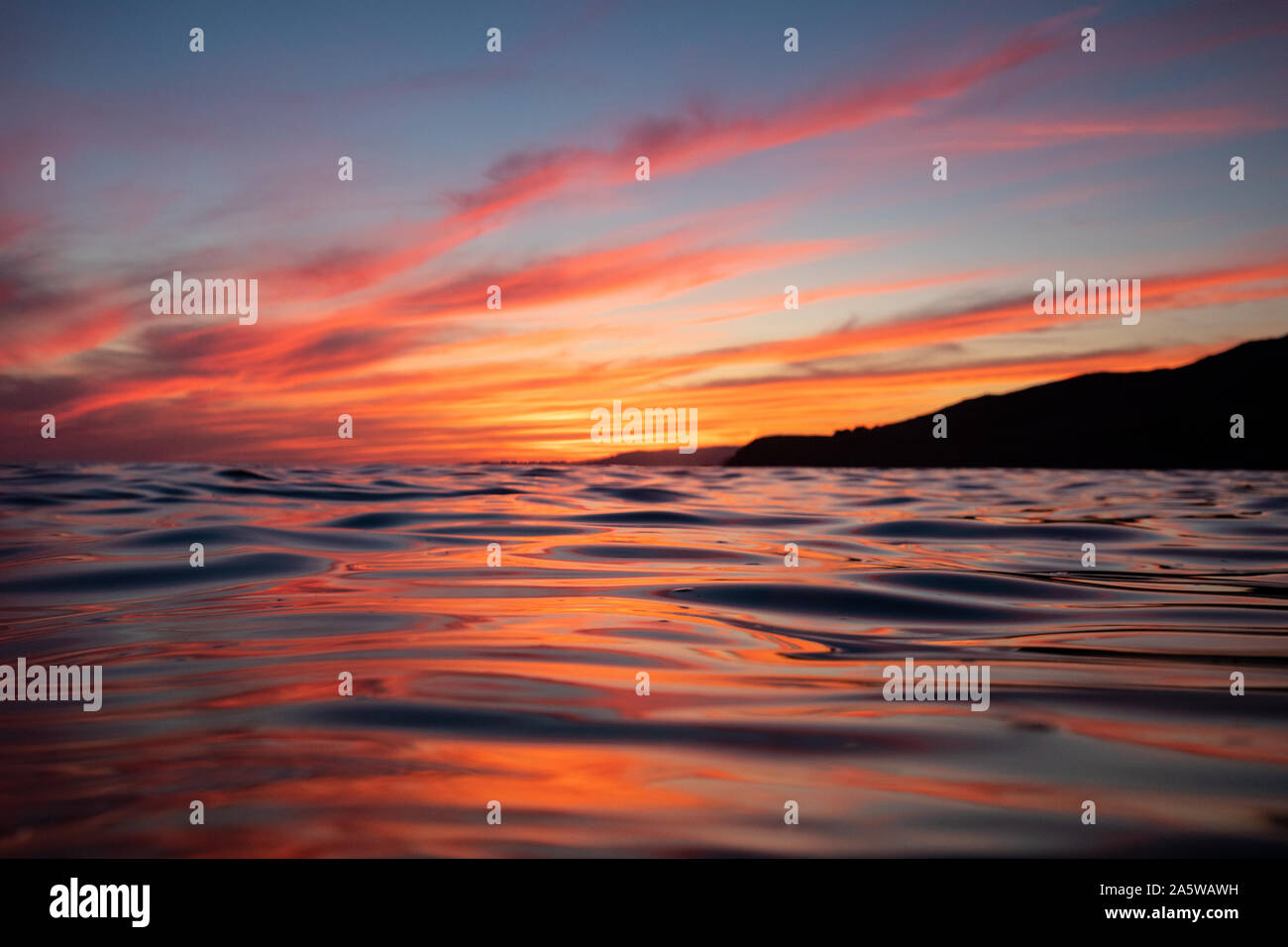 The ocean surface reflects vibrant sunset afterglow from colorful clouds. Stock Photo