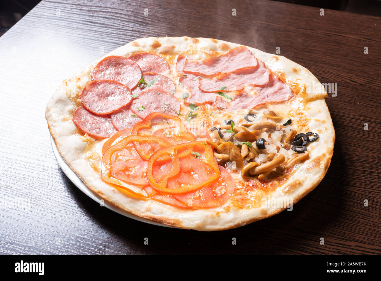 Cheap pizza 4 seasons. With ham, pepperoni, mushrooms, and tomatoes. Stock Photo