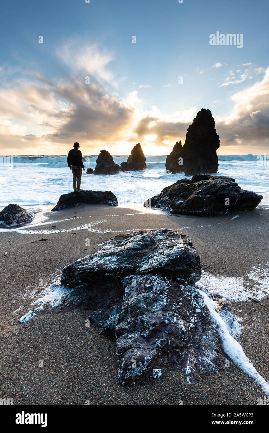 A man explores the sandy beach and rugged rocks of Rodeo Beach at sunset, a great day trip adventure from San Francisco. Stock Photo