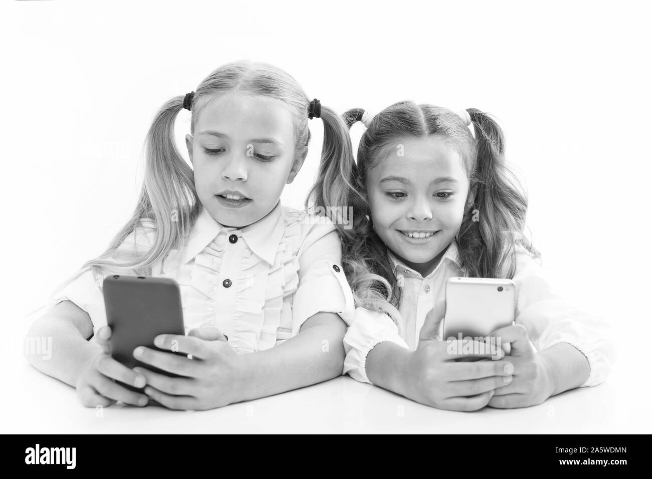 Smart pupils. Little pupils texting message during class isolated on white. Cute lyceum pupils diving deep into smartphone lessons. Small pupils using mobile phones in classroom. Stock Photo