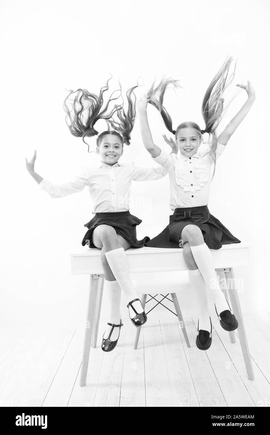 Healthier hair from root to tip. Adorable little girls with flying hair sitting on desk. Cute small children with long hair ponytails wearing school uniform. Luxurious hair extensions. Stock Photo