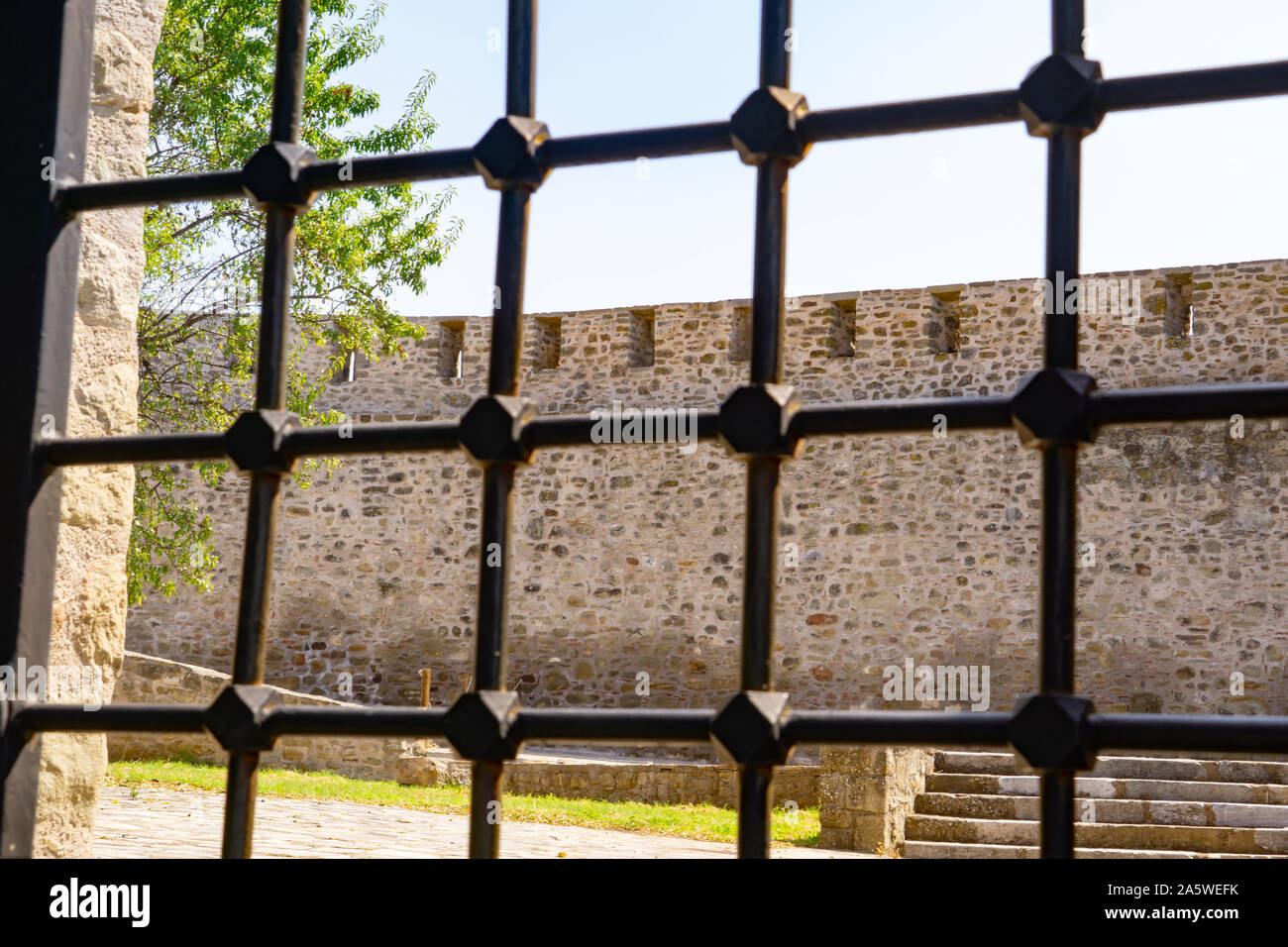 Through security grill to interiror wall of stone structure of Bizantine Trikala Castle in Greece. Stock Photo