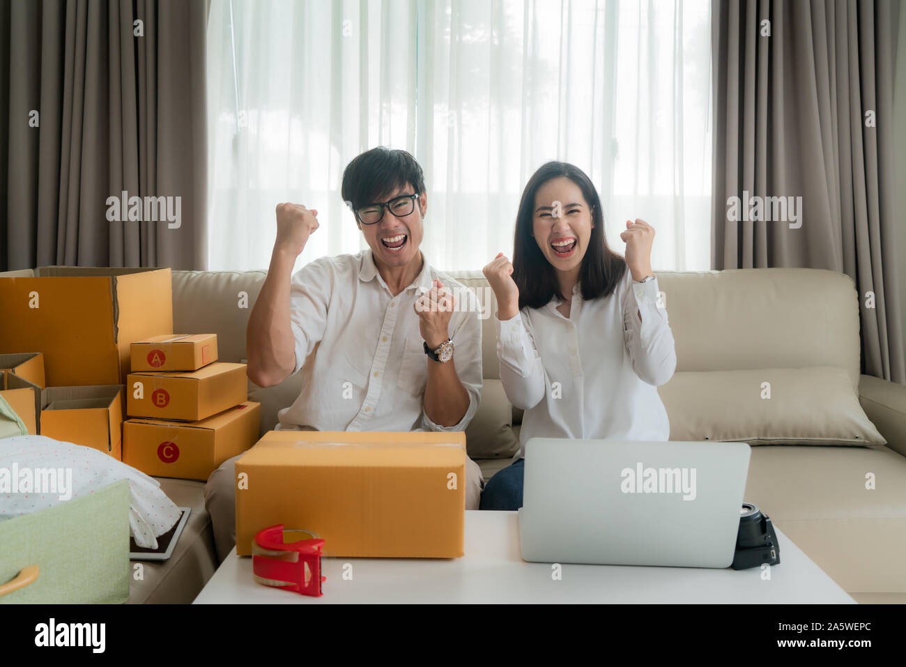 Asian man and woman are selling their online via on the computer in house and very satisfied when there are many of her orders. Small business startup Stock Photo