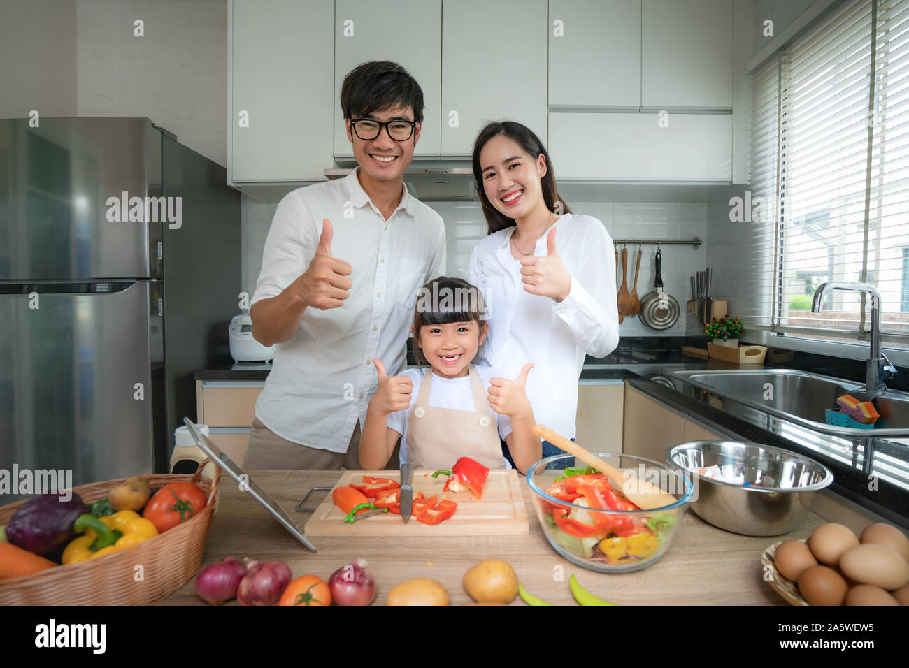 Asian family with father, mother and daughter shredded vegetable salad and thump up while the family was cooking in the kitchen at home. Family life l Stock Photo