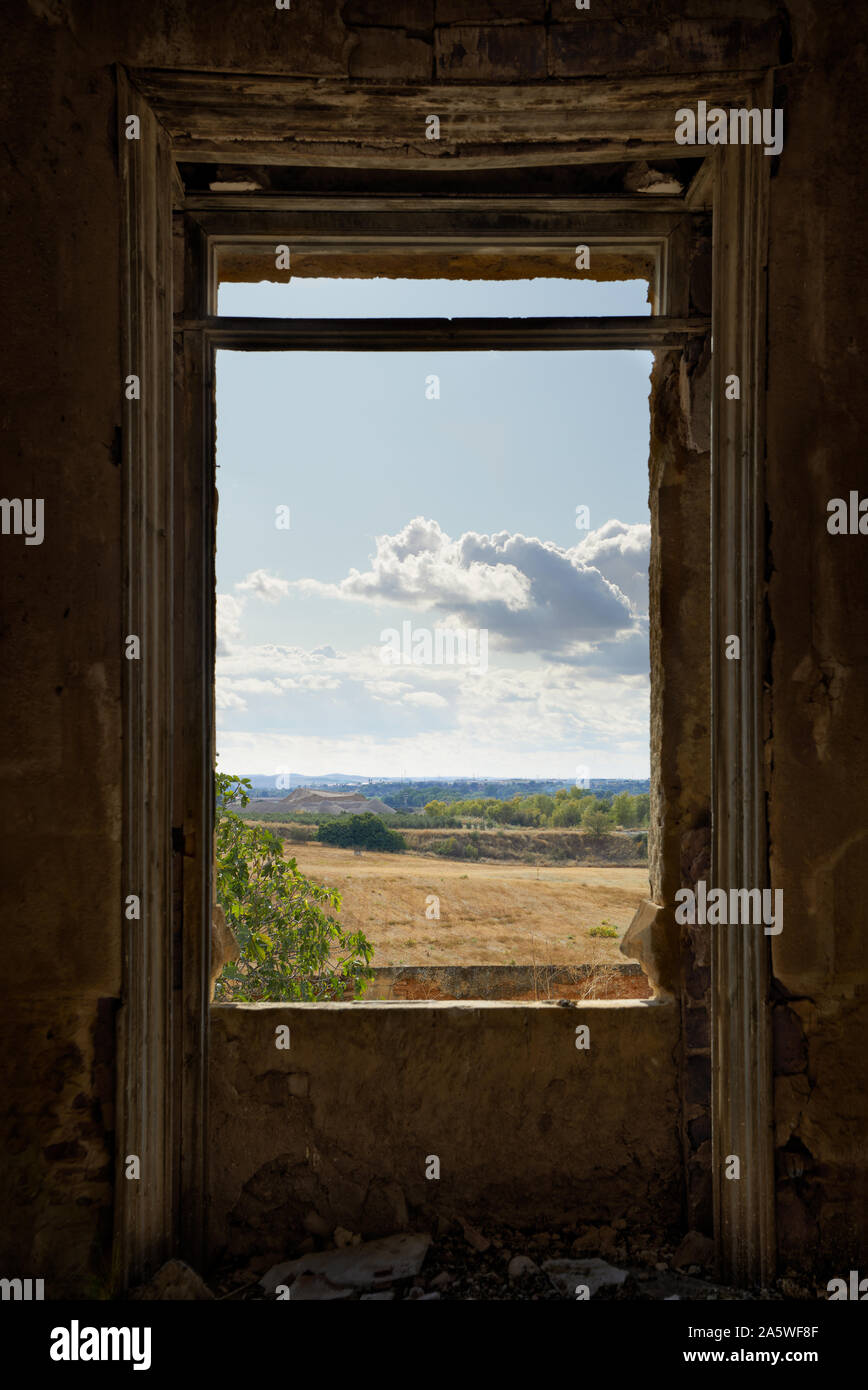 View of a meadow and cloudy sky through a dilapidated window Stock Photo