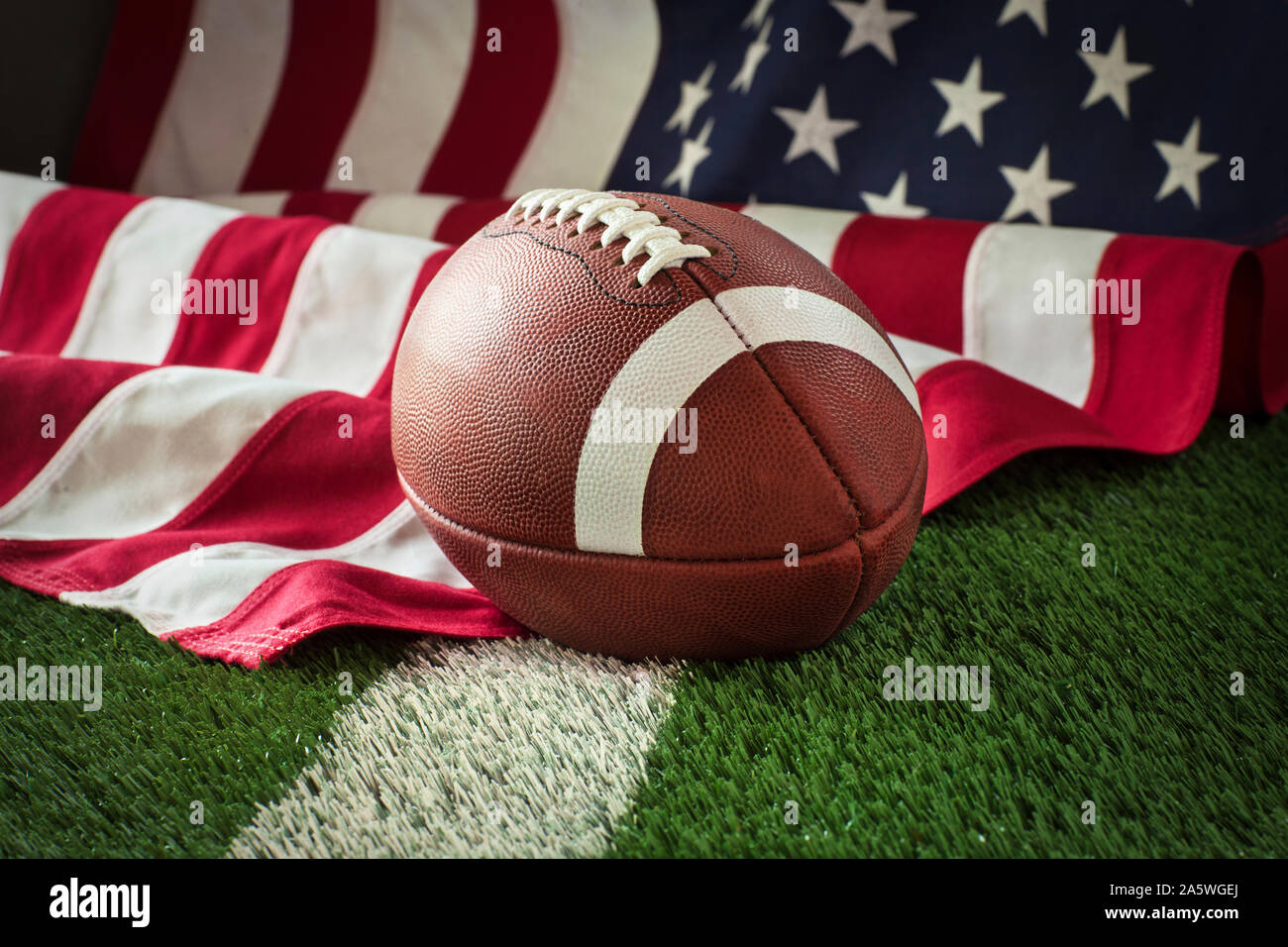 Football on a green field with white stripe and American flag behind Stock Photo