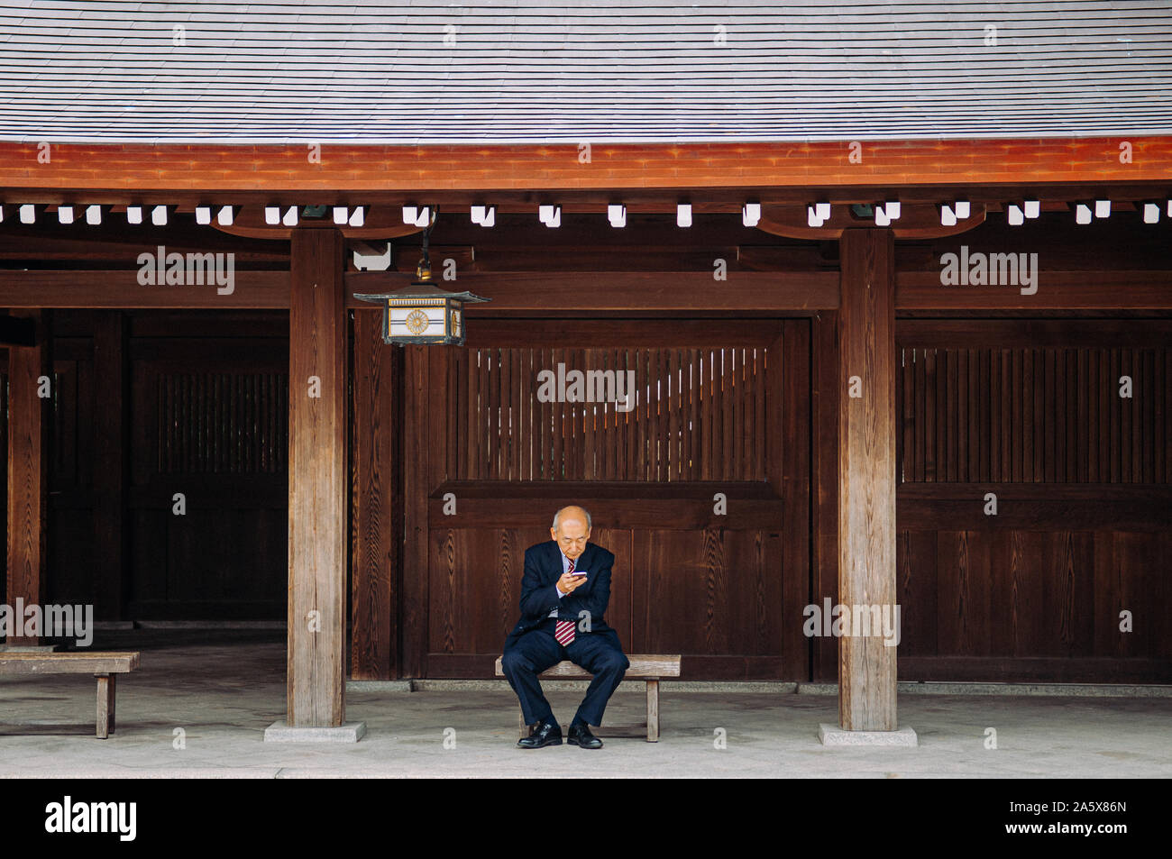 DEC 5, 2018 Tokyo, Japan - Meiji Jingu Shrine Historic Wooden corridor with  Asain senior guy sit on bench seat using smart phone - Most important shr Stock Photo