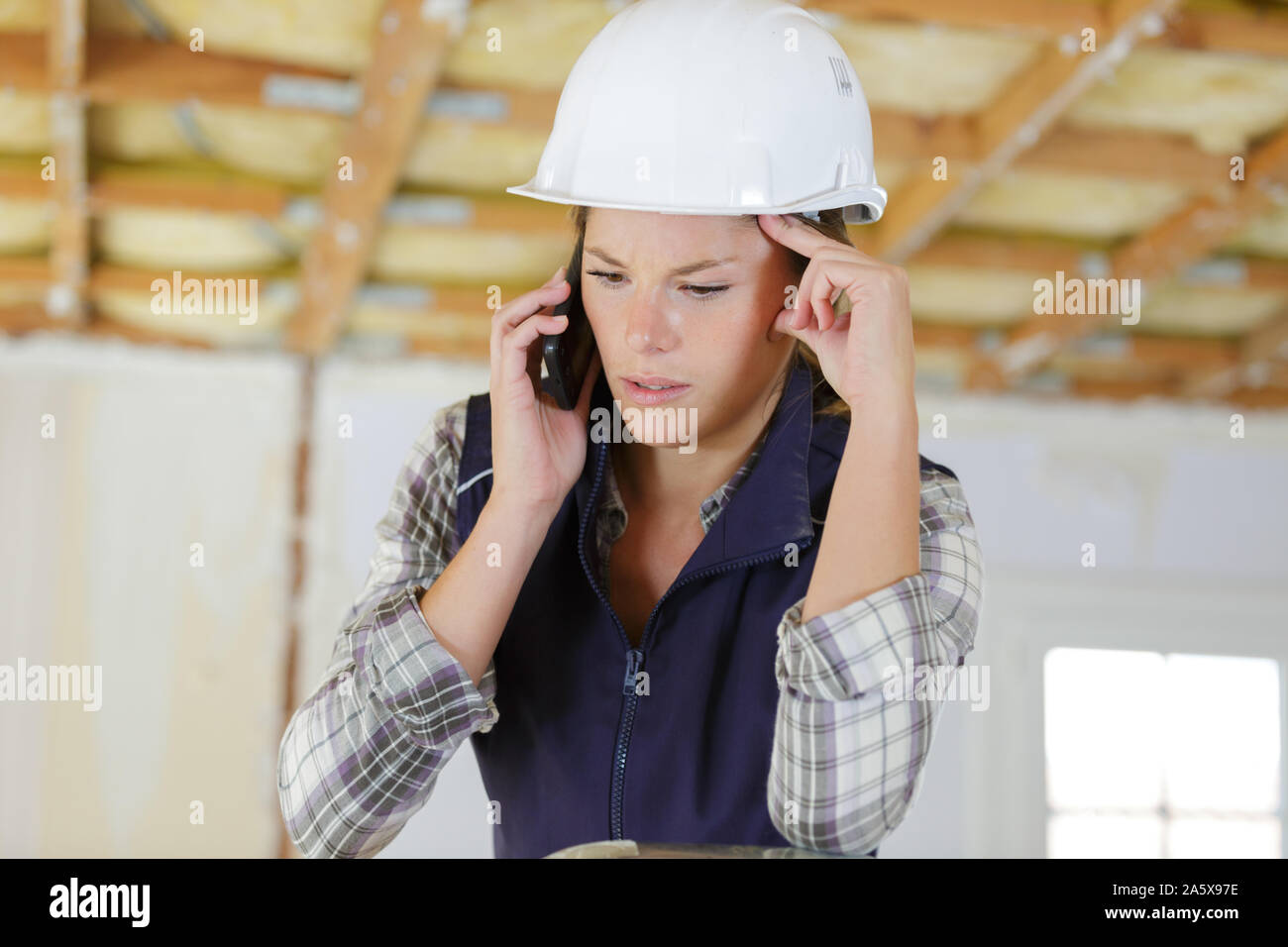 worried female builder using cellular telephone Stock Photo