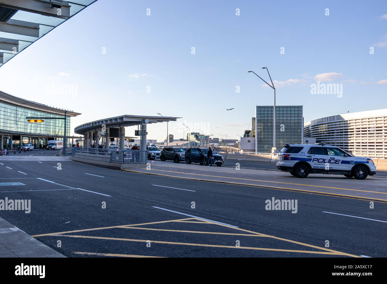 Terminal 1 at Toronto Pearson Intl. Airport on a busy, sunny afternoon - with a plane taking off in the background and police car parked in the median Stock Photo