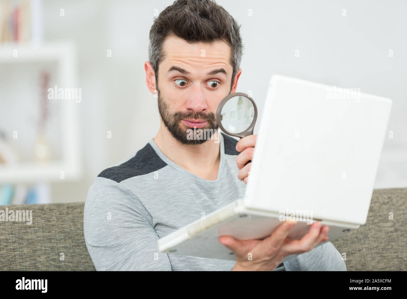 handsome man looking at his laptop through manifying glass Stock Photo
