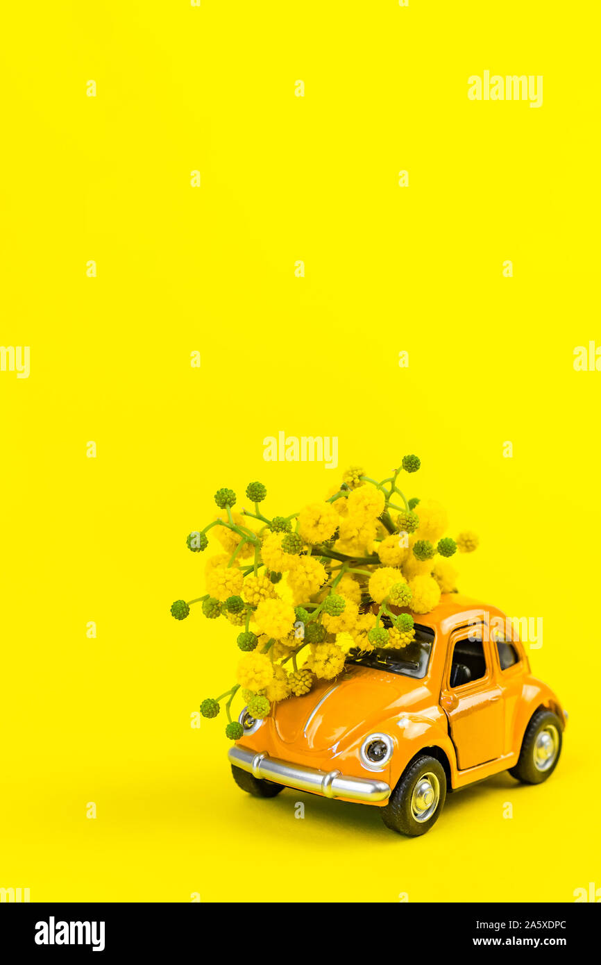 Moscow, Russia - February 23, 2019: 8 March International Women's Day card with toy model of retro car delivering bouquet of mimosa flowers on yellow Stock Photo