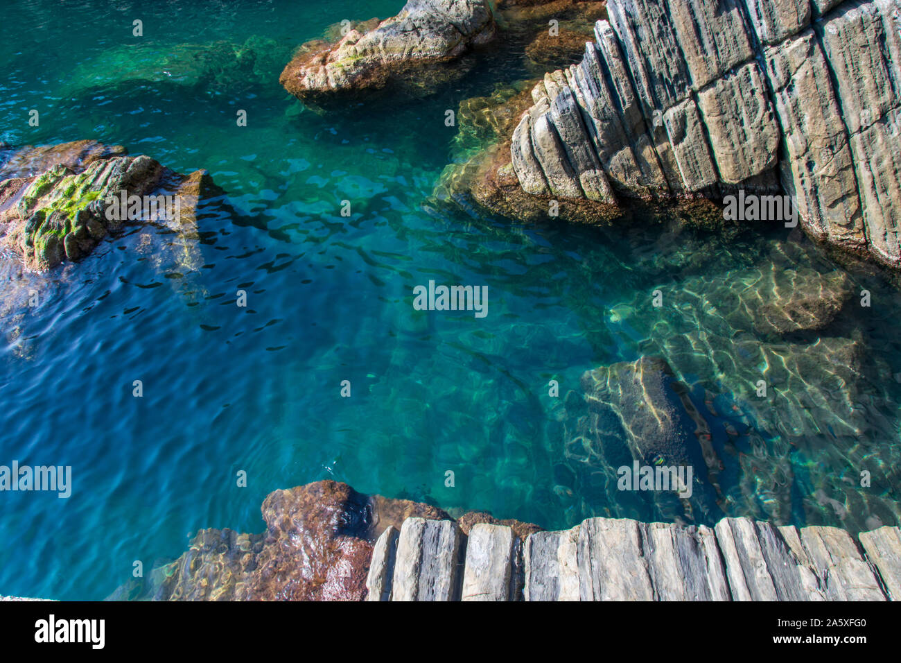 The turquoise water seen among the rocks in the city of Riomaggiore, Cinque Terre, La Spezia, Italy Stock Photo