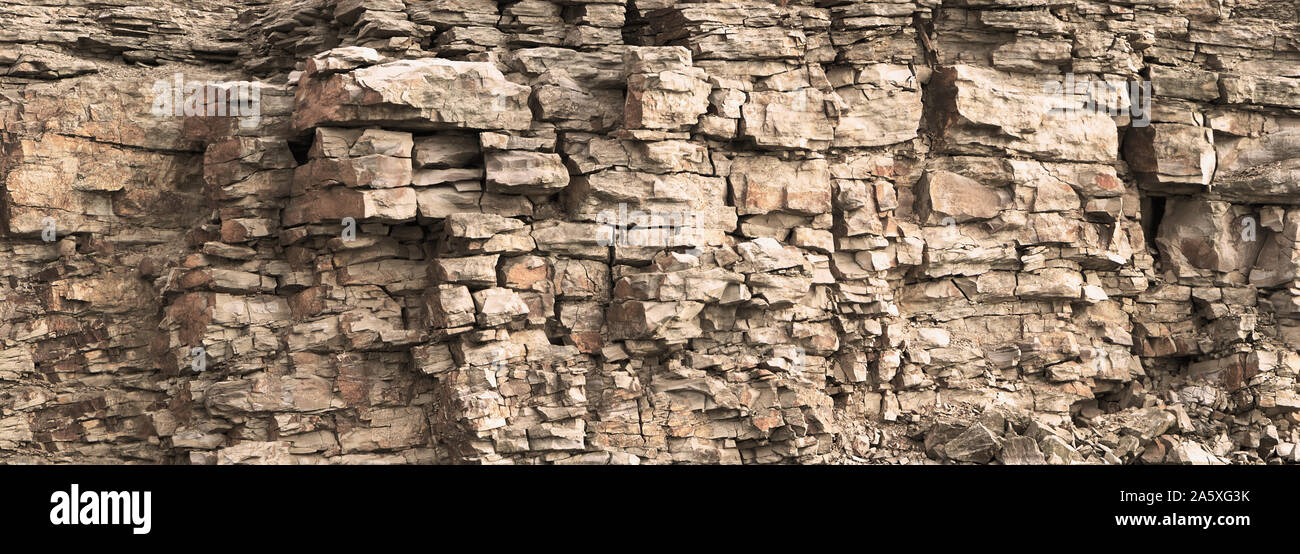 Rock cliff face background. Toned. Wild stone protruding crumbling layered blocks in quarry. Abstract texture for stone mining industry. Copy space Stock Photo