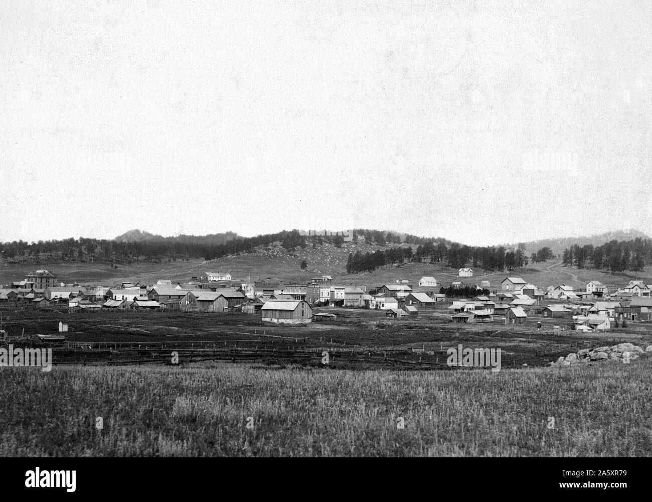 Distant view of small town; field in foreground and hills in background. Stock Photo