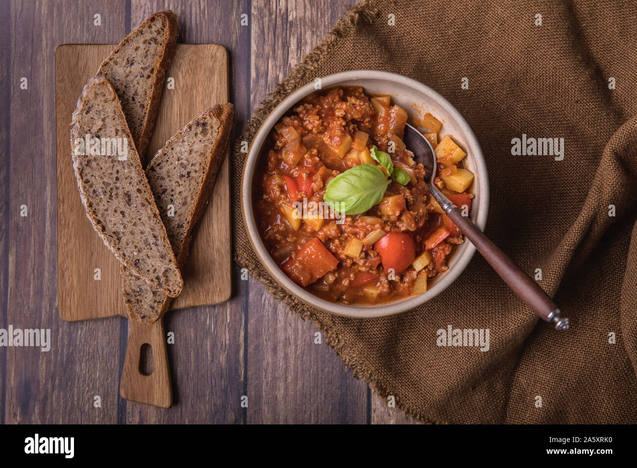 Thick soup or broth with minced meat, potatoes, tomatoes and red bell peppers. Next to the soup are some slices of homemade sourdough bread and fresh Stock Photo