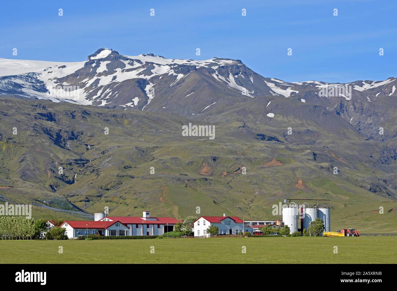 Farm located at the foot of a mountain in the middle of green meadows below the glaciated Eyjafjallajokull Volcano, Suourland, Sudurland, South Stock Photo