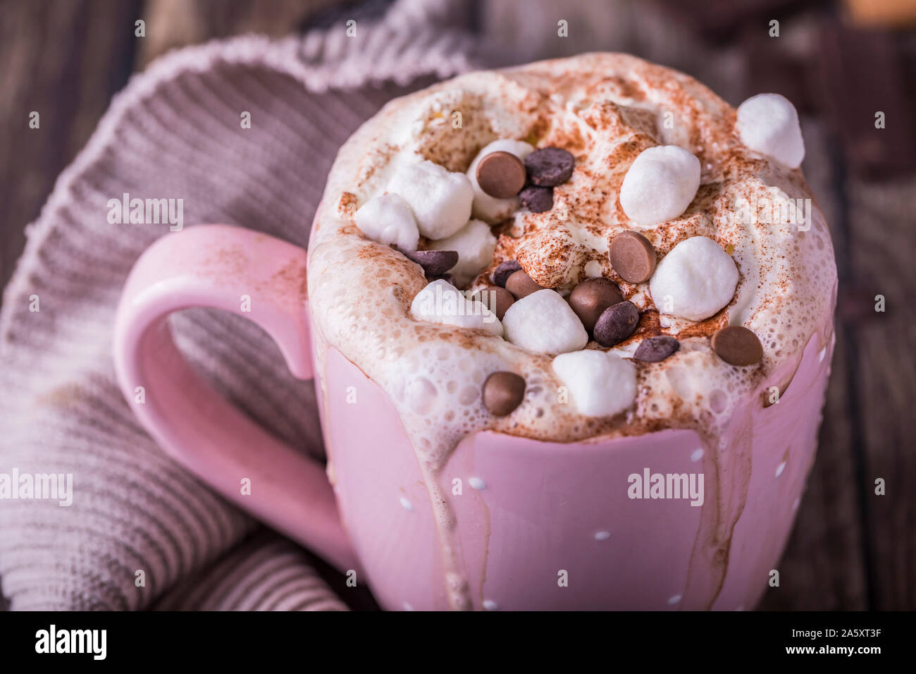 Close-up of a pink mug with lush hot chocolate with whipped cream and pieces of marshmallows and chocolate chips. Stock Photo