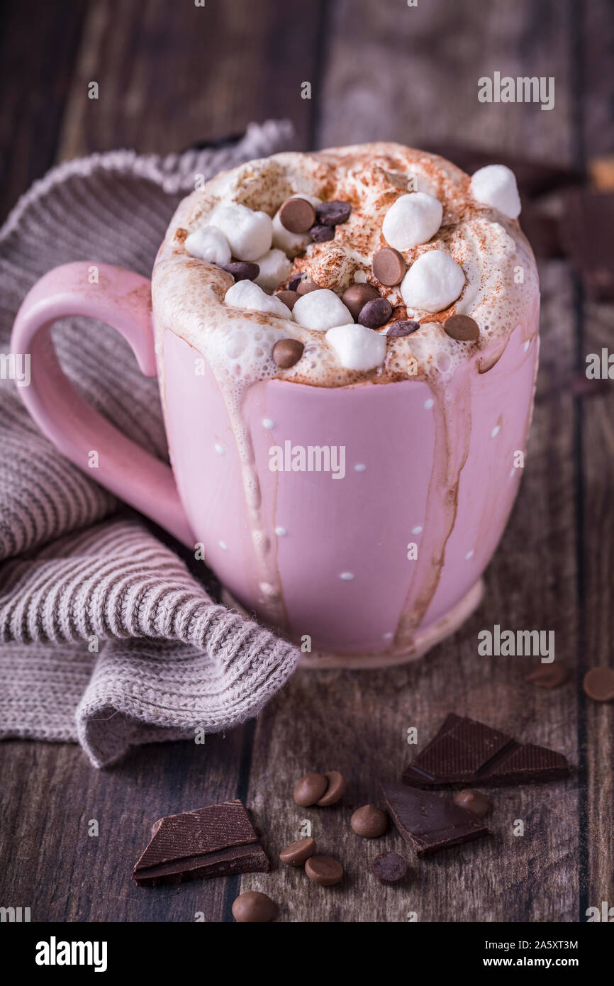 A pink mug with luxurious hot chocolate with whipped cream. On top of the cream are pieces of marshmallows and chocolate chips, and there are pieces o Stock Photo