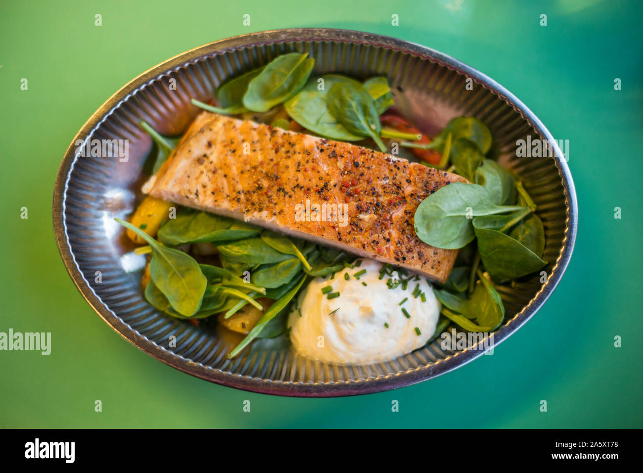 A healthy low carb meal of grilled salmon,  baby spinach leaves and yoghurt sauce in a metallic bowl. Green background, from above perspective. Stock Photo
