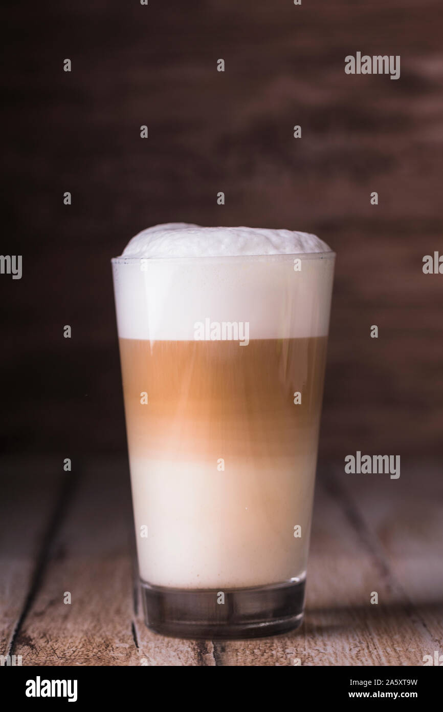Coffee cafe latte macchiato in a high glass on a wooden background. There is copy space next to the glass, and the photo is horizontal. Stock Photo