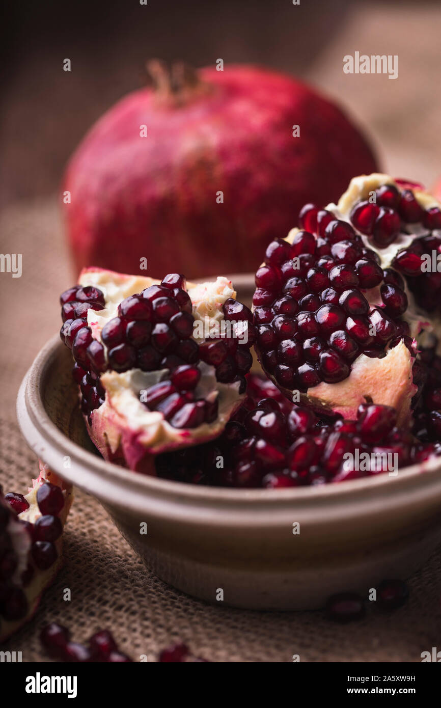 Pomegranate slices and seeds in a ceramic bowl. The fruits are on a rustic jute textile, and there are also some pomegranate seeds next to the bowl. V Stock Photo