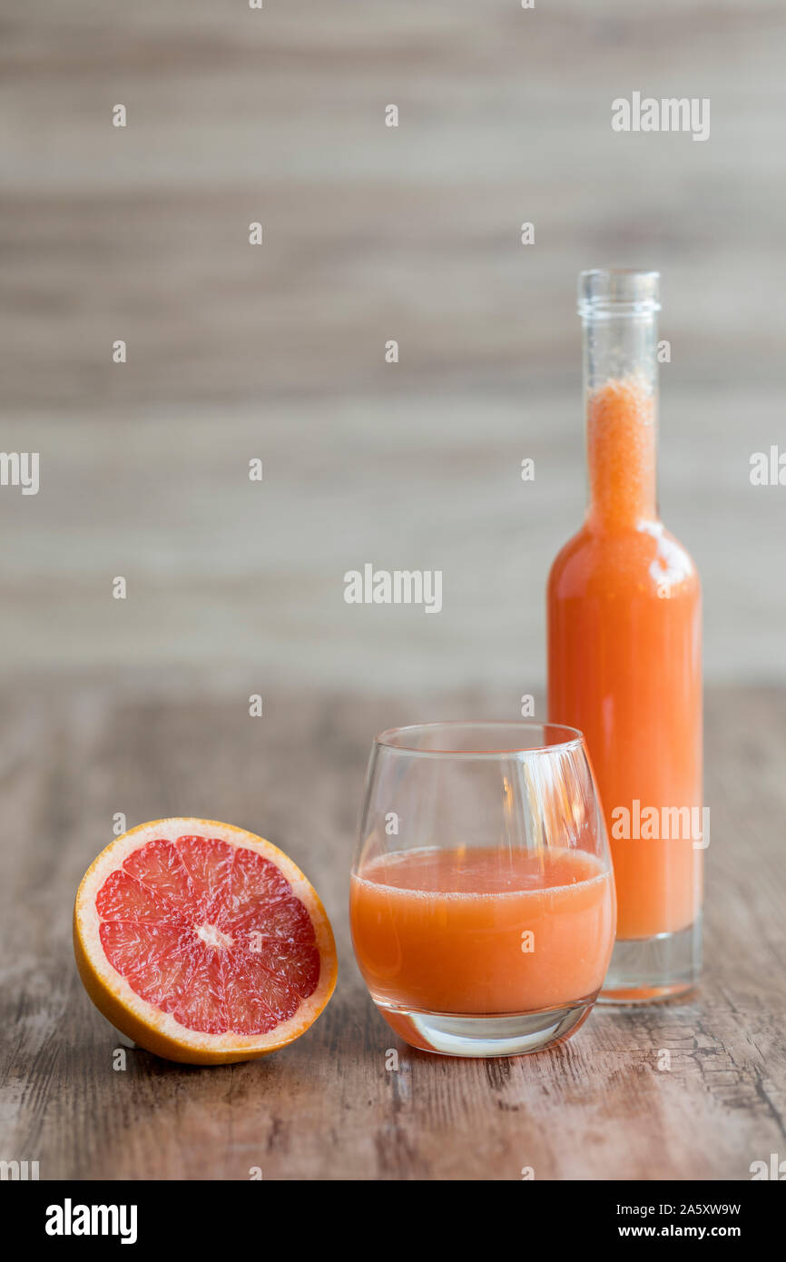A glass of fresh, healthy organic grapefruit juice  on a wooden table. There is a bottle of the  juice in the background, and a halved pink grapefruit Stock Photo