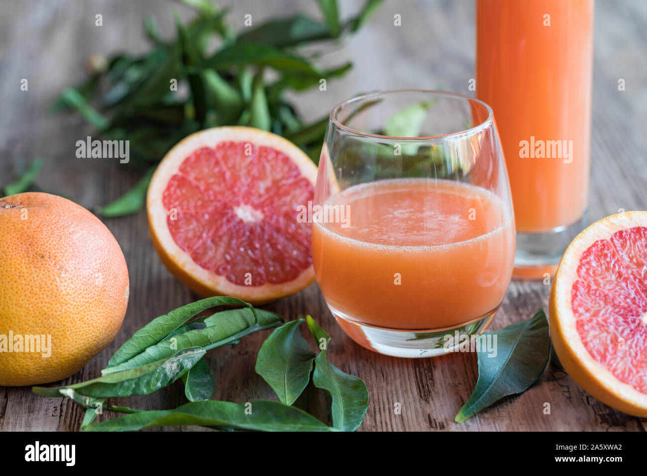 A glass of fresh, healthy organic grapefruit juice on a wooden table. There is a bottle of the grapefruit juice in the background. A halved pink grape Stock Photo