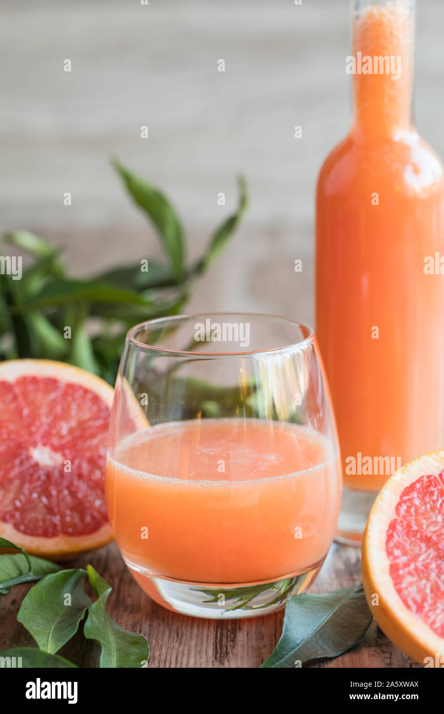 A glass of fresh healthy organic grapefruit on a wooden table. There is a bottle of the grapefruit juice in the background. A sliced pink grapefruit a Stock Photo