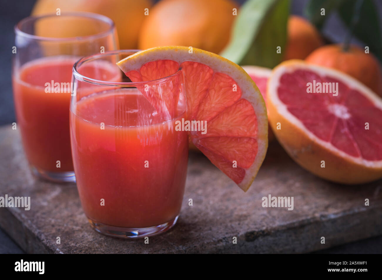 Healthy organic blood orange juice with blood grapefruit and oranges on a dark stone surface. Dark background, with defocused fruit leaves. Stock Photo