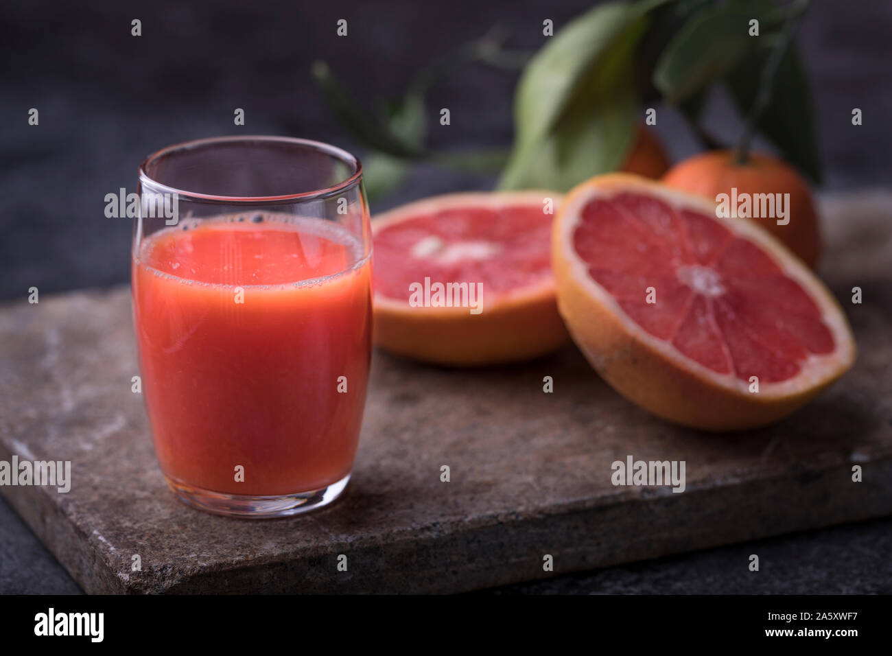 Healthy organic blood orange juice with blood grapefruit and oranges on a dark stone surface. Dark background, with defocused fruit leaves. Stock Photo