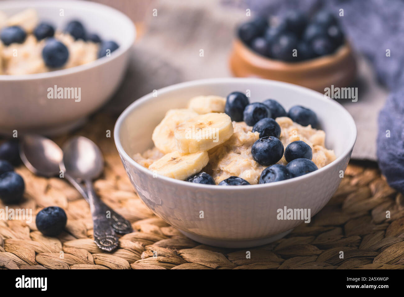 Healthy oatmeal porridge breakfast with fresh blueberries and sliced bananas. There are two bowls in the photo, one partly out of the frame, and two v Stock Photo