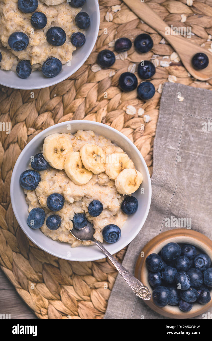 Healthy oatmeal porridge breakfast with fresh blueberries and sliced bananas. There are two bowls in the photo, one partly out of the frame, and two v Stock Photo