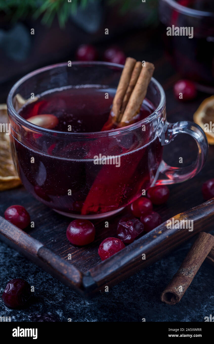 Mulled wine with cinnamon sticks, dried oranges and cranberries. The glasses are on a dark wooden tray with a green pine tree branch in the background Stock Photo