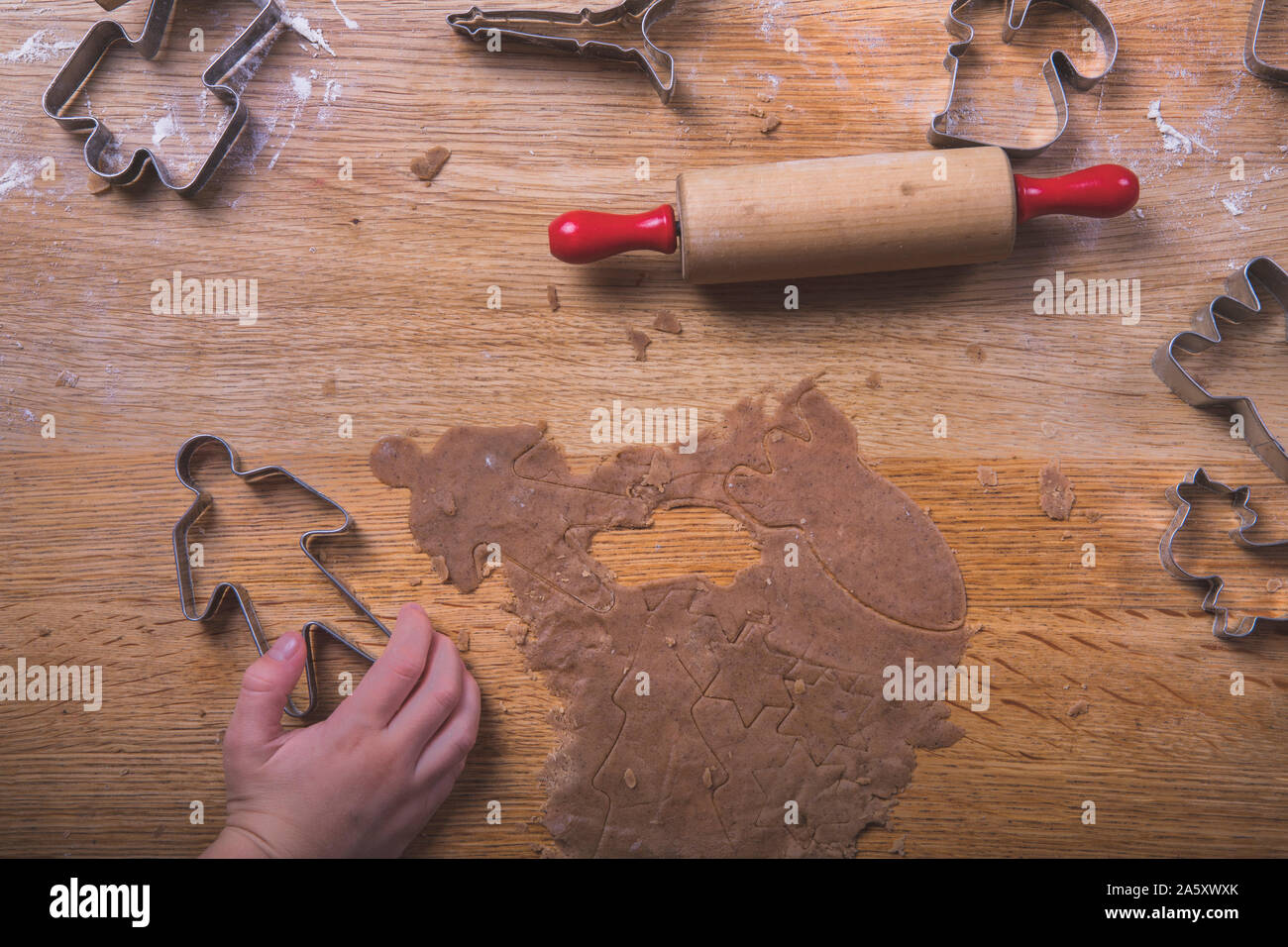 Gingerbread baking on a wooden table, with a kids hand grabbing one of the cookie cutters.  There are cookies cutters in various shapes on the table, Stock Photo