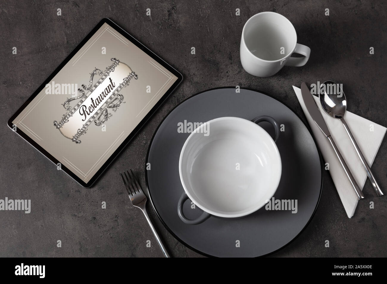 Tablet with stylish restaurant logo and laid table Stock Photo