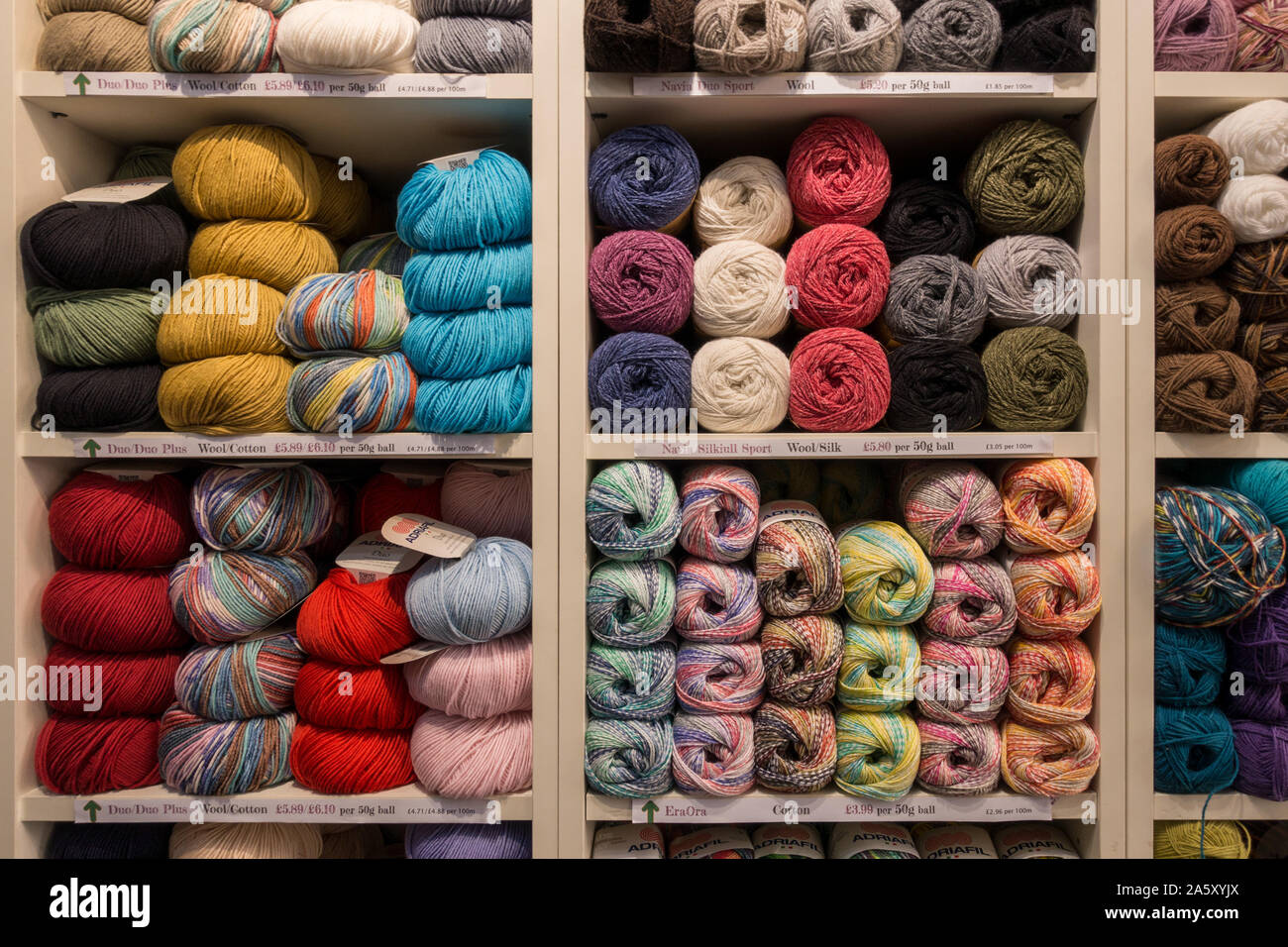 Display of colourful balls of wool stacked on shelves in 'Stitch Upp' sewing and knitting haberdashery shop, Uppingham, Rutland, England, UK Stock Photo