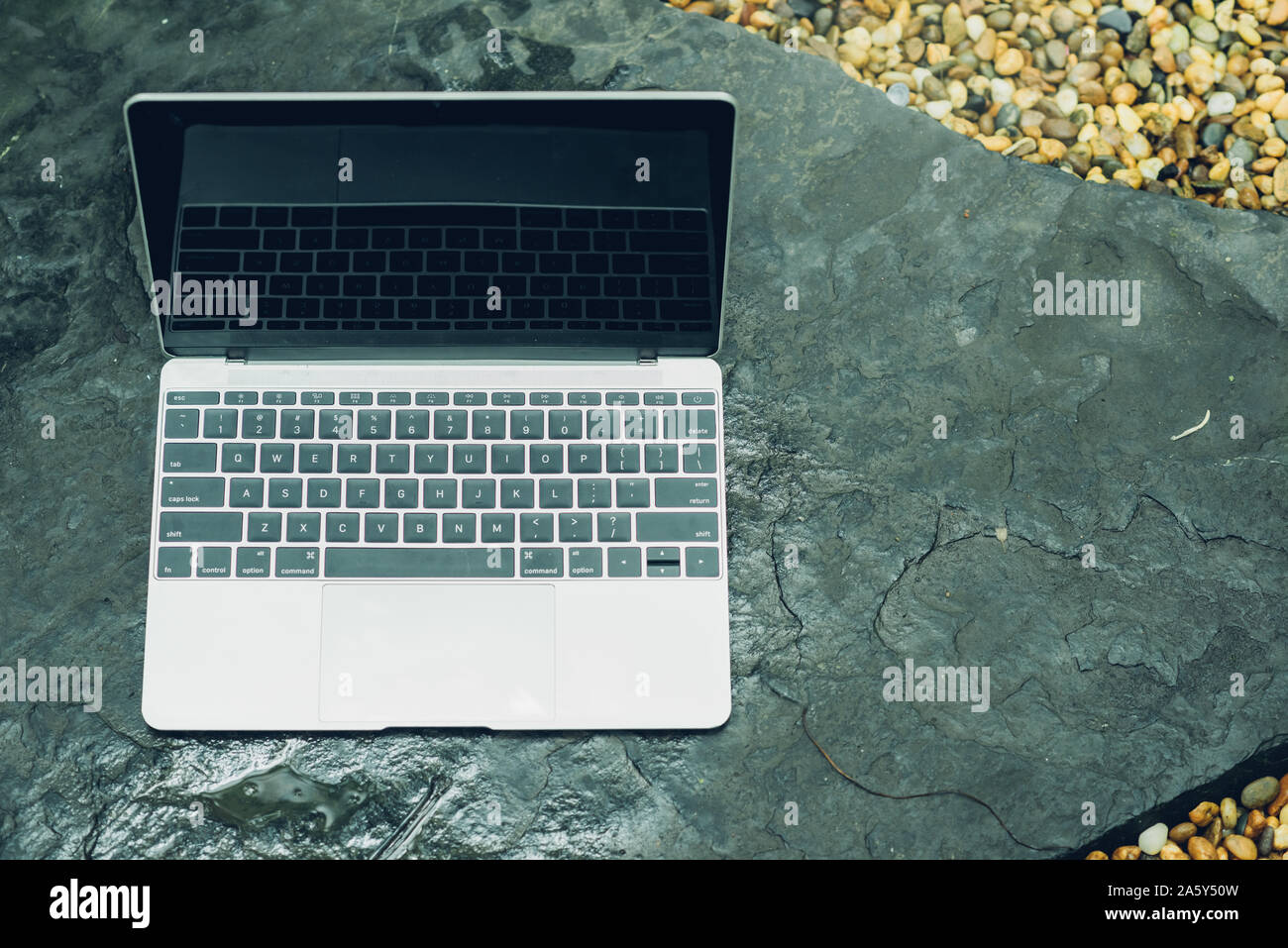 Laptop computer mockup has empty screen outside on stone in garden of coffee shop. Stock Photo
