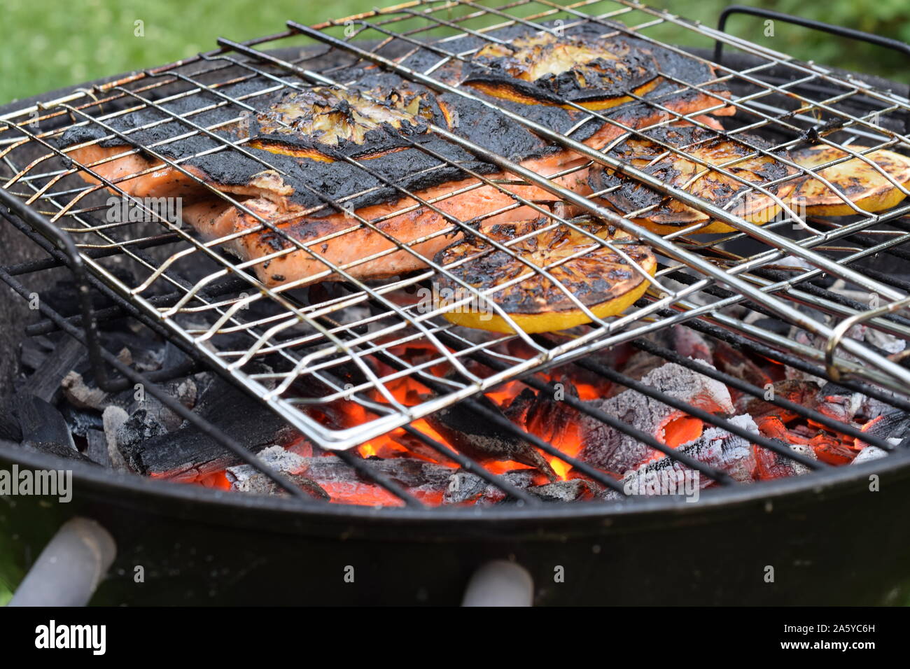 Grilling whole salmon fillets with gridiron. Fish and lemon slices are reaydy to eat. Skin is burned, but meat inside is ripe and juicy. Stock Photo