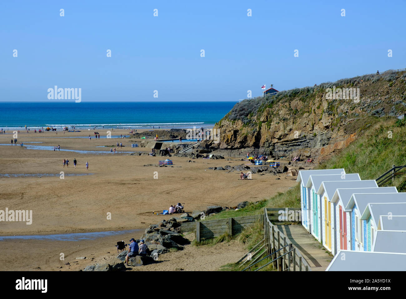 Multi coloured beach huts with boardwalk facing the beach at Bude