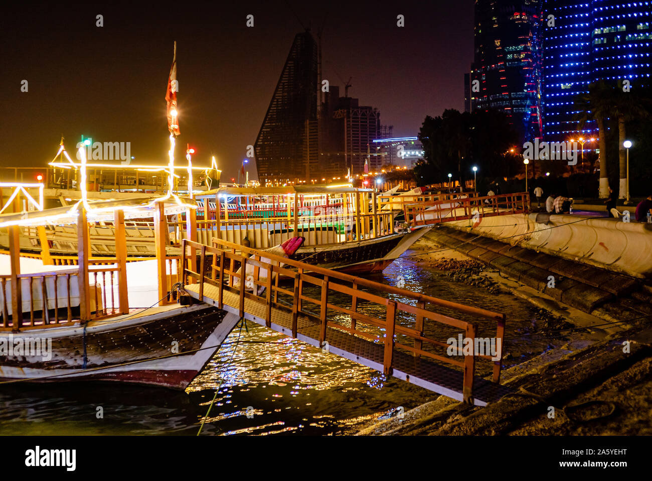 Wooden dhow boats, fitted with light strips, sit waiting for hire late in the evening on Doha's Corniche Stock Photo