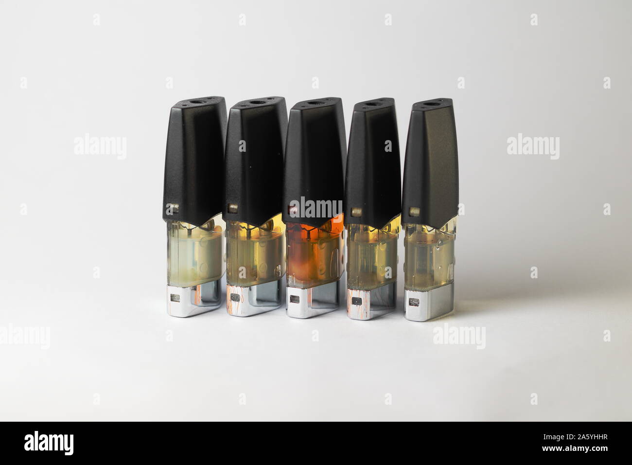 e-juice vape refill pods with liquids of different shades of orange yellow, white background isolated close up Stock Photo