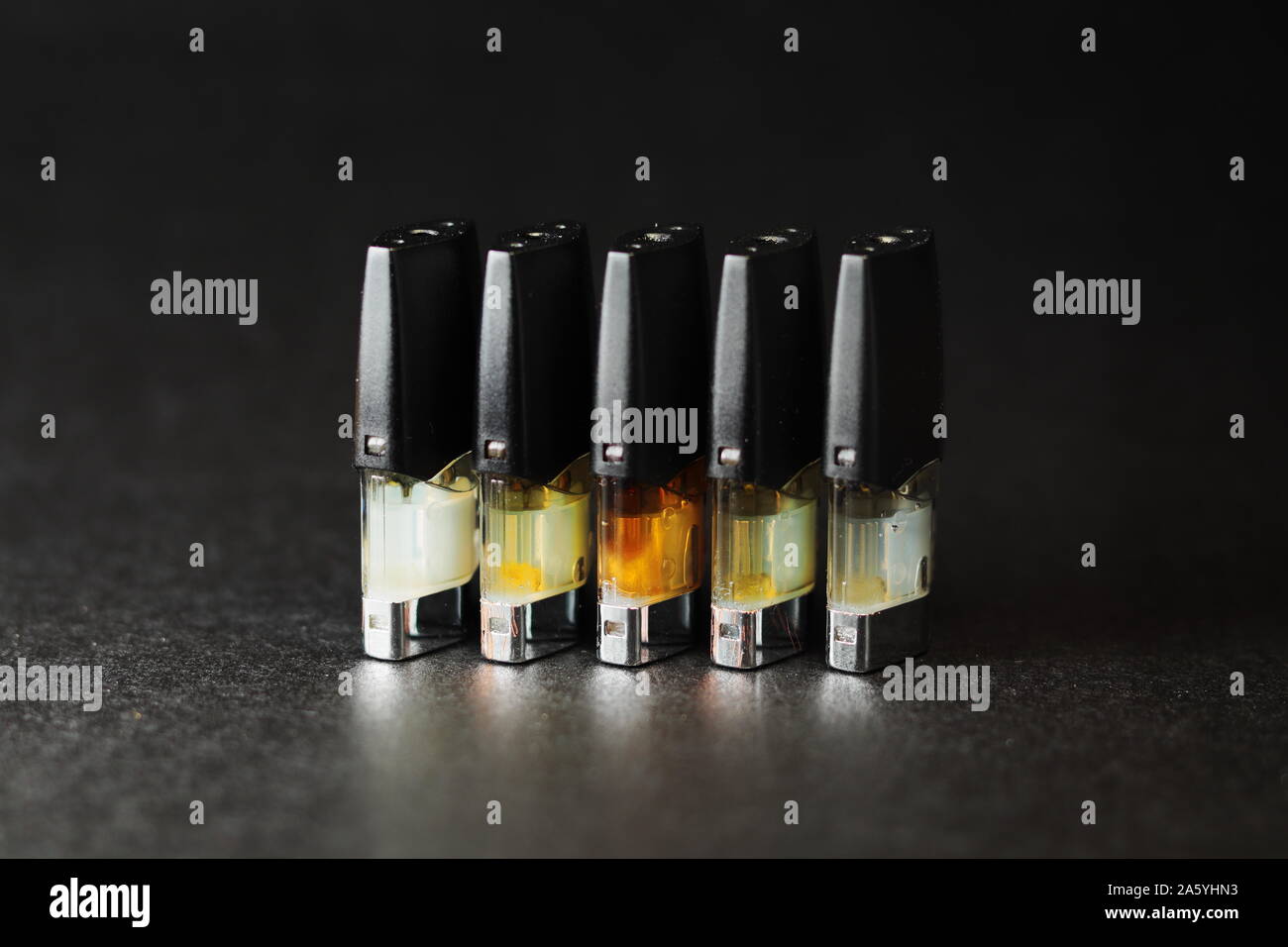 e-juice vape refill pods with liquids of different shades of orange yellow, black background isolated close up Stock Photo