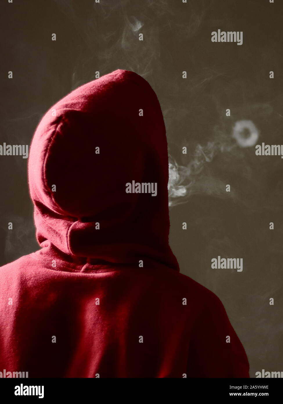 Young male in red hoodie vaping smoking, blows a single smoke ring, isolated rear view Stock Photo