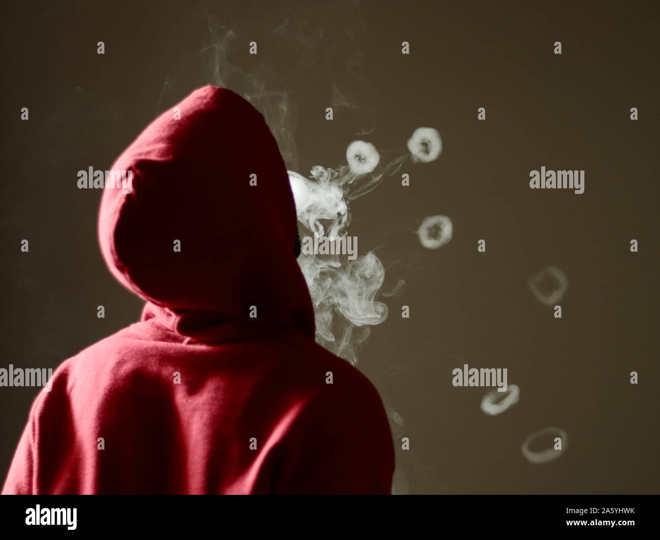 Young male in red hoodie vaping smoking, blows many smoke rings, isolated rear view Stock Photo